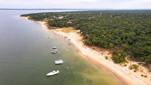 An aerial view of a coastal area with boats docked along the shore, surrounded by dense forest and a sandy beach.