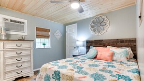 A bedroom with a bed, dresser, ceiling fan, decorative wall art, and a window with blinds.