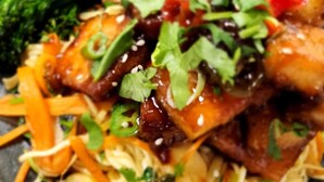 Ein Gericht mit Nudeln, Gemüse und Fleisch, garniert mit Sesamsamen und Kräutern.