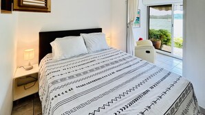 Ein Schlafzimmer mit Bett, Nachttisch, Lampe und einem Fenster mit Blick ins Freie.