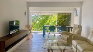 Ein Wohnzimmer mit Fernseher, einem Glastisch, einer Couch und einem Essbereich mit Stühlen und Tisch.