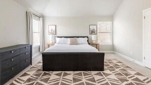 A bedroom with a large bed, a dresser, two bedside tables, and a patterned rug. - Pool-Hot Tub-Putting Green-Arcade-Oasis (Austin)