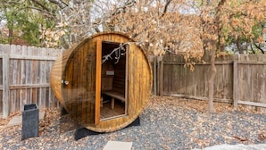 A wooden cylindrical structure with an open door, surrounded by a wooden fence and gravel ground. - Pool-Hot Tub-Putting Green-Arcade-Oasis (Austin)