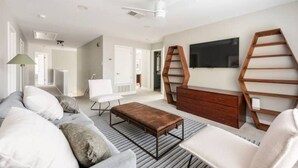A modern living room with a sofa, coffee table, TV, and a unique wooden ladder shelf. - Pool-Hot Tub-Putting Green-Arcade-Oasis (Austin)