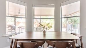 A dining area with a large table and six chairs, large windows with blinds, and a view of the outdoors. - Pool-Hot Tub-Putting Green-Arcade-Oasis (Austin)