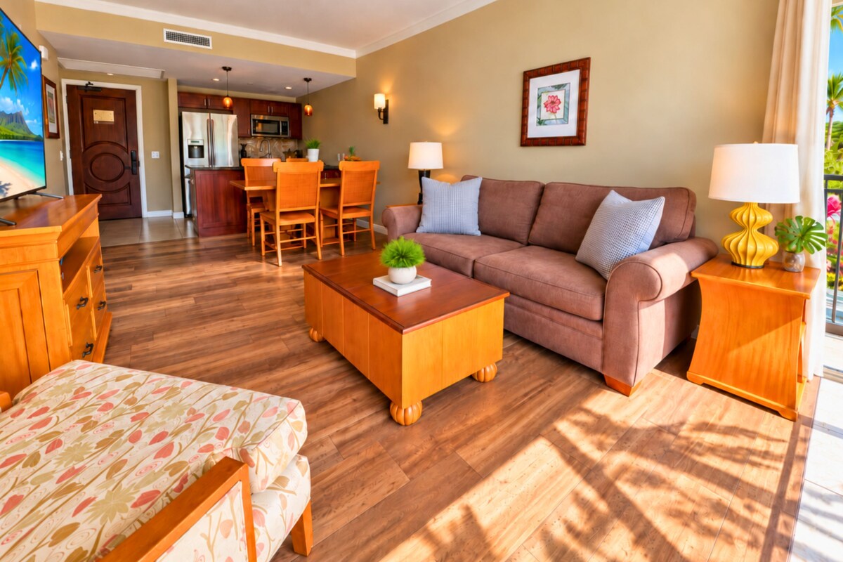 Une chambre d’hôtel avec un plancher en bois, un canapé, une table basse agrémentée d’une plante, une télévision et un coin repas avec des chaises et une table.