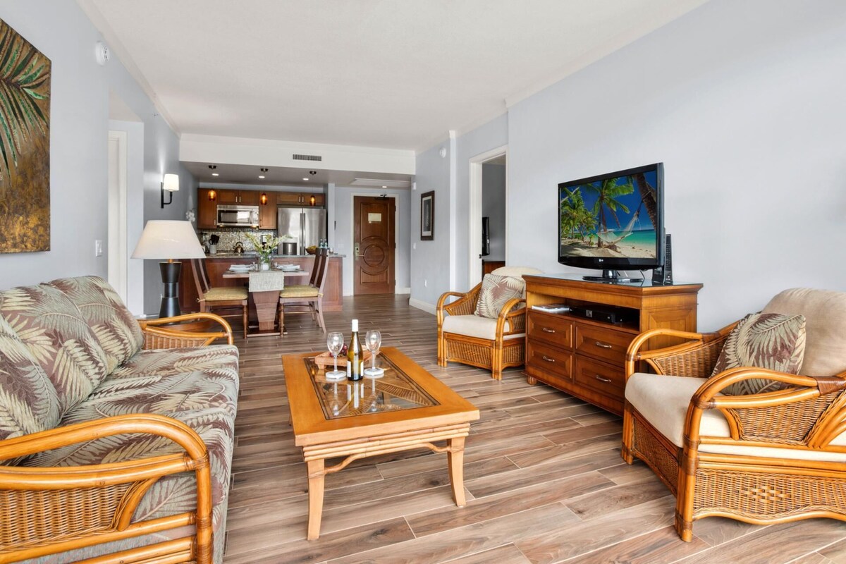 Un salon avec des meubles en osier, une table basse en bois et un téléviseur posé sur un meuble en bois.