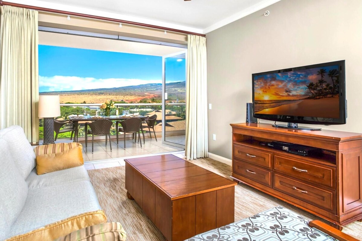 Une chambre d’hôtel avec un balcon, un canapé, une table basse, une télévision et une armoire en bois.