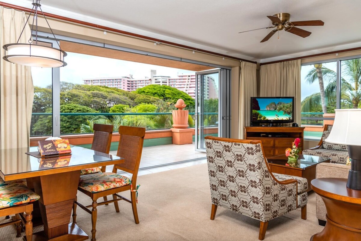 Une chambre d’hôtel avec un balcon, un coin repas, une télévision et un ventilateur de plafond.