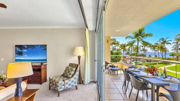 A balcony with a dining table set, a chair, and a TV displaying a beach scene.