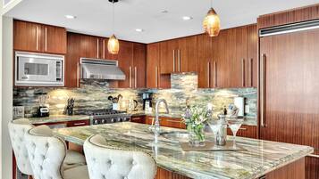 A modern kitchen with wooden cabinets, a central island with seating, a built-in microwave, a stove, and pendant lighting.