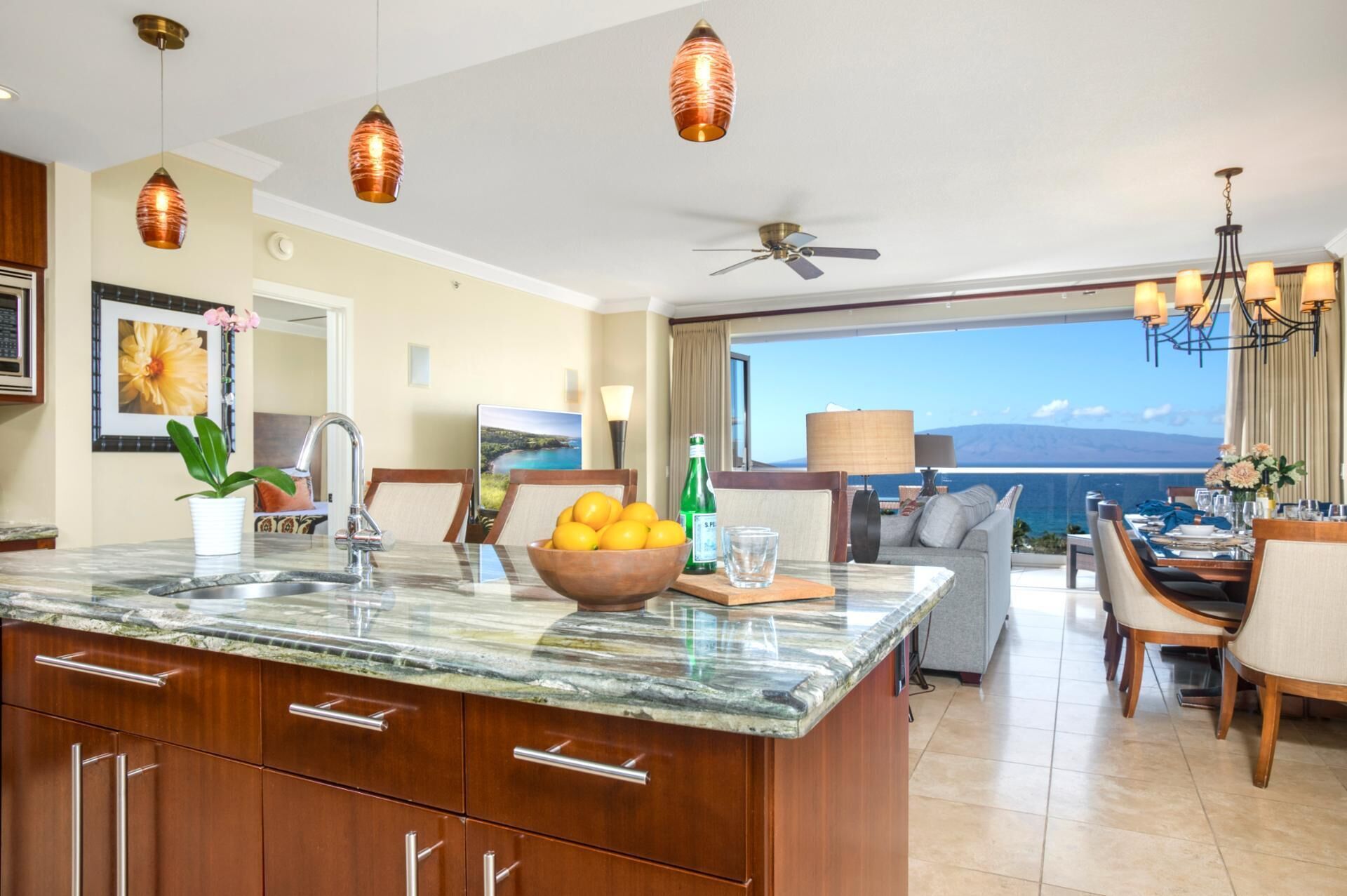 A modern kitchen with a marble countertop, wooden cabinets, and a dining area with a view of the ocean.