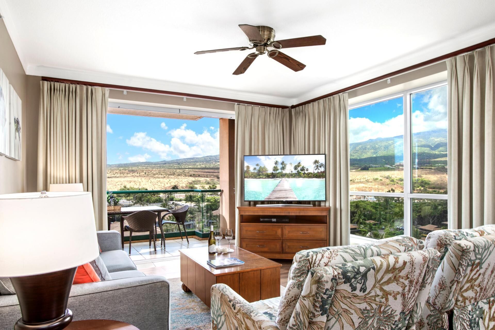 Une chambre d’hôtel dotée d’une grande télévision, d’un canapé, d’une table basse et d’un balcon offrant une vue sur le paysage.