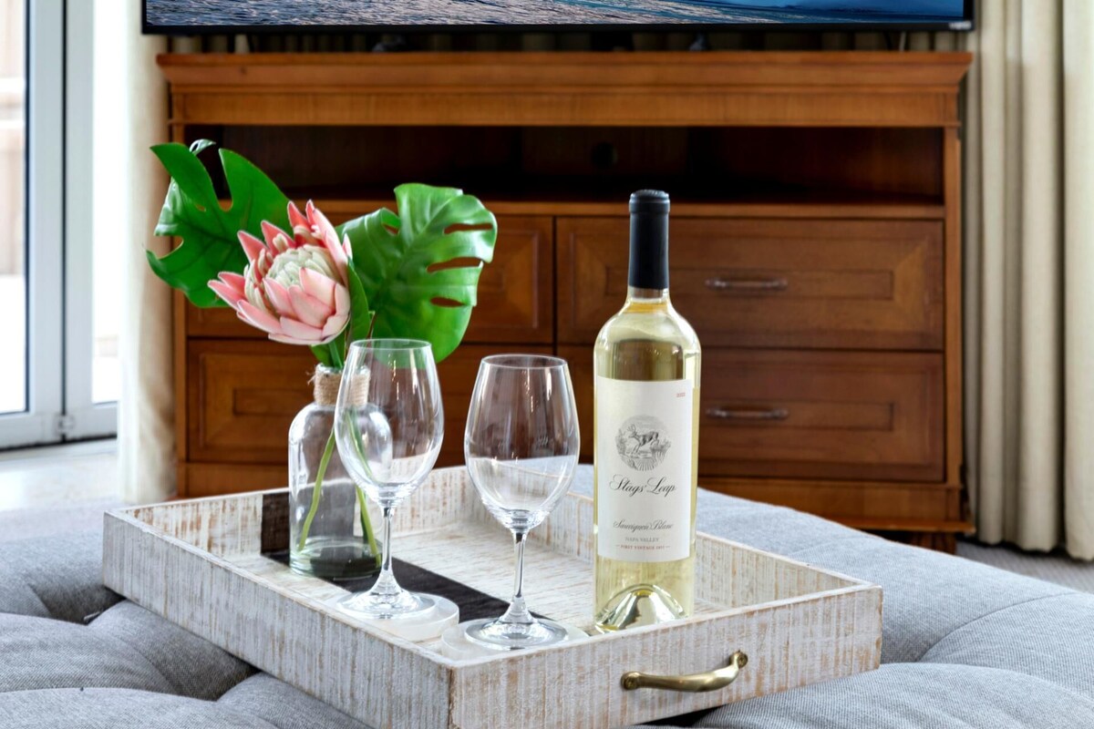 Un plateau avec une bouteille de vin, deux verres et un vase de fleurs, le tout posé sur une surface texturée.