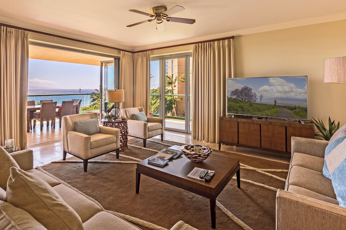 A spacious living room with a large TV, comfortable seating, and a view of the ocean.