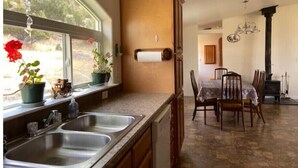 Une cuisine dotée de deux éviers, d’une fenêtre ornée de plantes, d’un meuble en bois et d’un coin repas avec des chaises et une table.