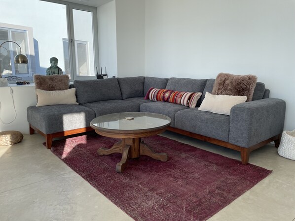 Ein modernes Wohnzimmer mit einem grauen Ecksofa, einem runden Glastisch und einem roten Teppich.