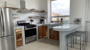 Eine moderne Küche mit einem Edelstahlkühlschrank, einem Gasherd, Holzschränken, einem großen Fenster und einem Barhocker.