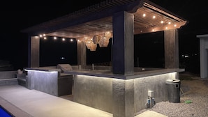 Ein Außenbereich mit Bar, einer Pergola, Sitzgelegenheiten und einem Pool.