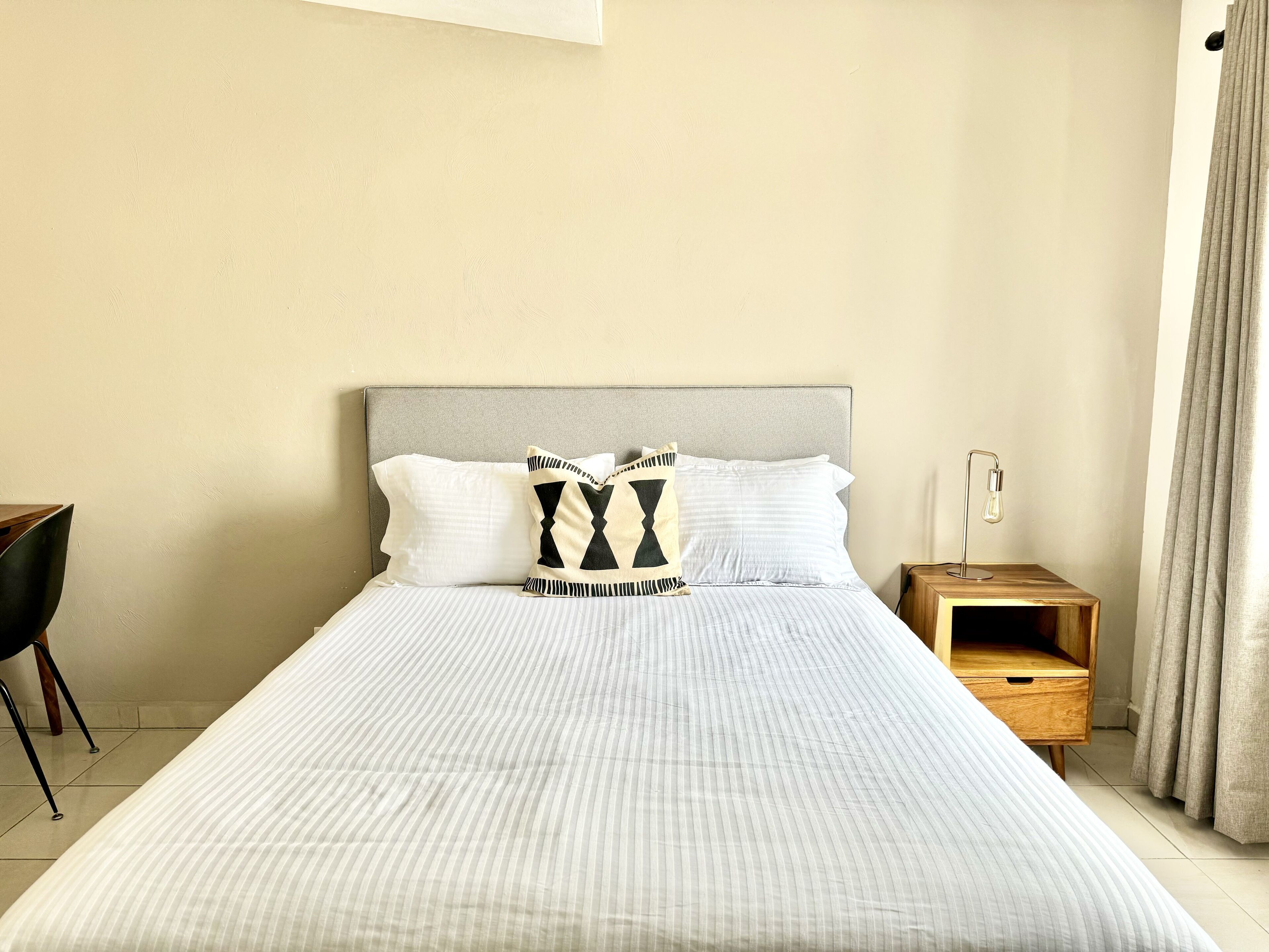 A neatly made bed with striped bedding, a grey headboard, and two decorative pillows.