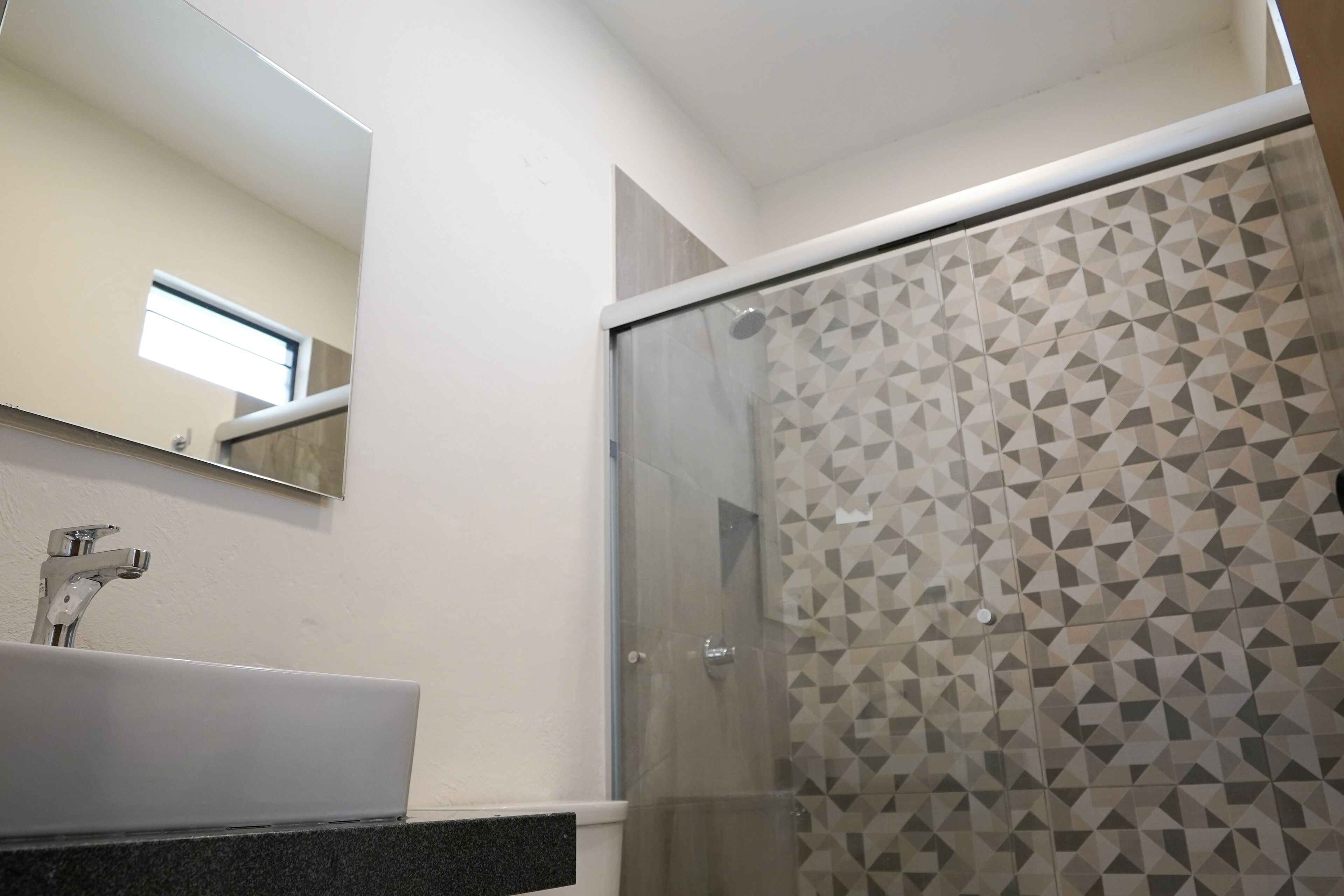 A modern bathroom with a glass shower enclosure, a white sink, and a geometric-patterned shower wall.