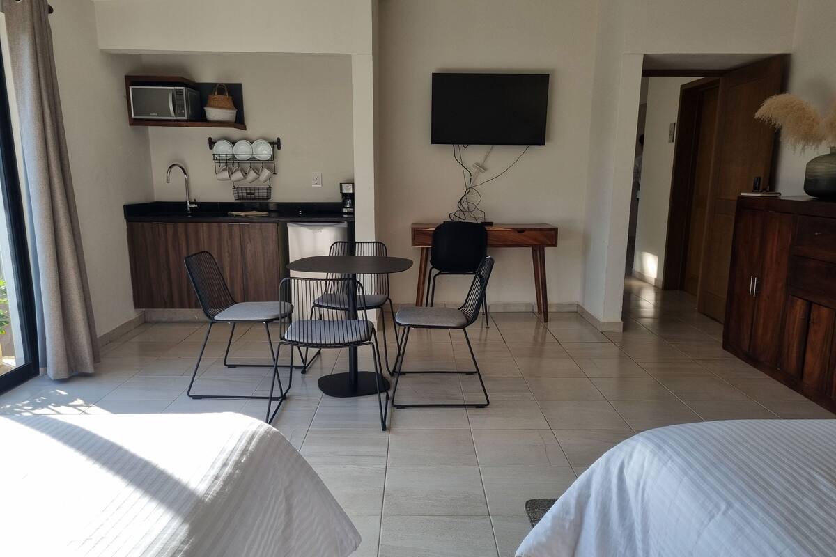 A modern hotel room with a dining area, kitchenette, and a TV mounted on the wall.