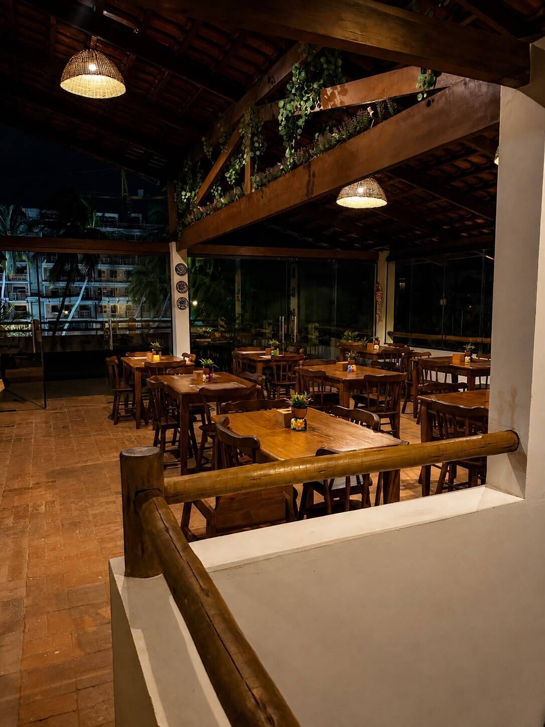 An indoor dining area with wooden tables and chairs, a staircase, and hanging plants.