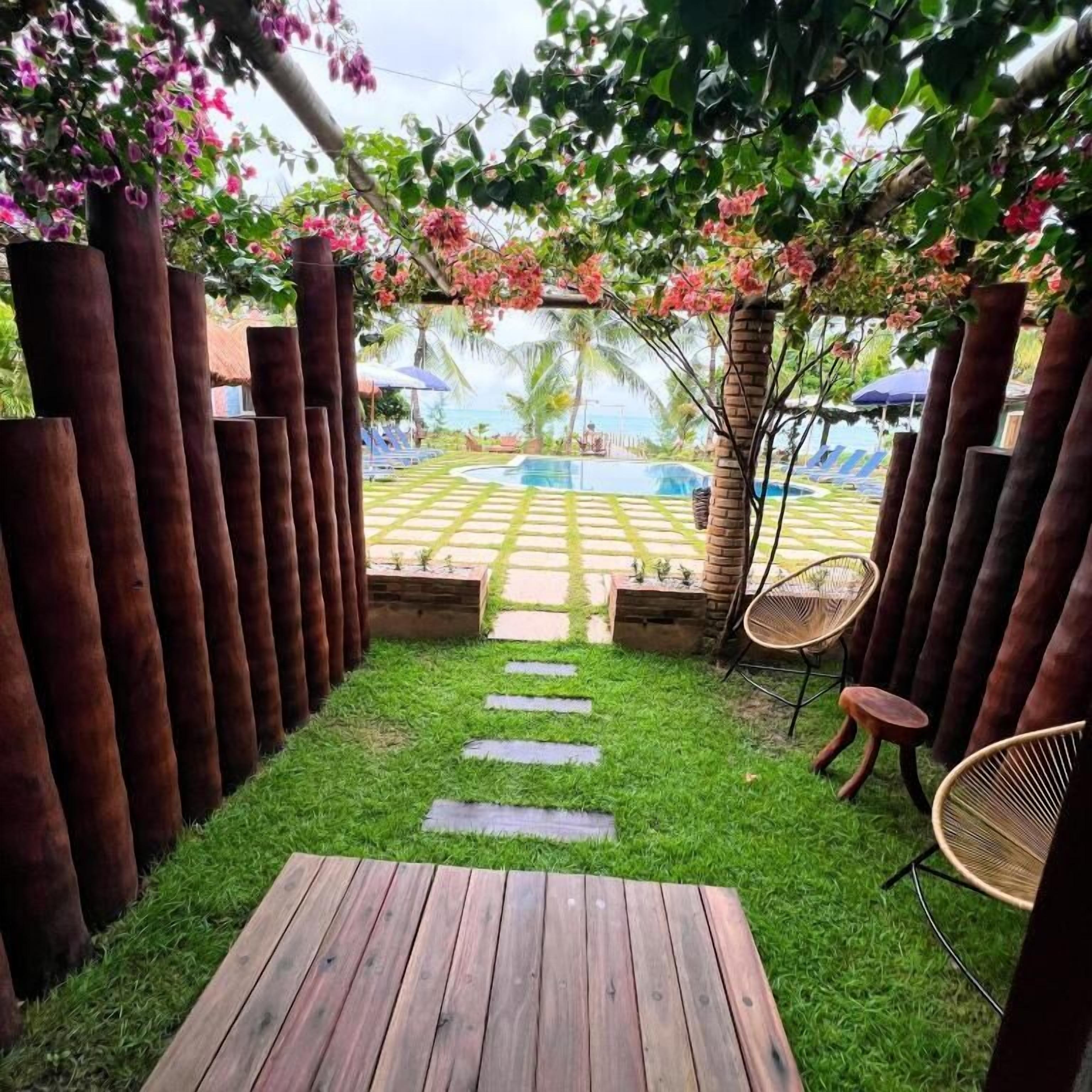 Een houten terras met een gazon, een zwembad en ligstoelen.