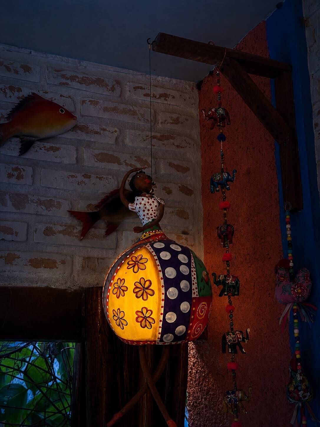 Una habitación con pared de ladrillo, un adorno colgante con forma de pez y una lámpara de colores.