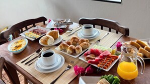 Ett frukostbord med tallrikar fyllda med mat, en kaffekopp och en kanna med apelsinjuice, placerat framför en vacker utsikt som syns genom ett fönster.