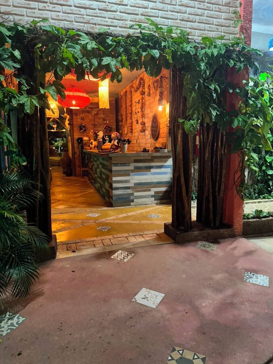 An entrance with a brick wall, a wooden structure with hanging lights, and a tiled floor with decorative patterns.