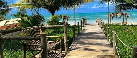 A wooden boardwalk leading to a beach with palm trees and a clear blue sky.