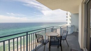 A balcony with a view of the ocean, a table, and two chairs.