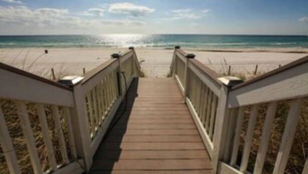 A wooden boardwalk leading to a beach with a clear sky.
