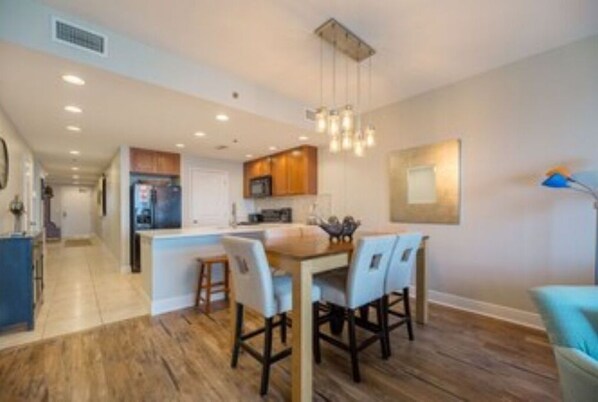 A modern kitchen with wooden flooring, a central island with chairs, and recessed ceiling lighting.