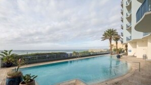 A swimming pool with a view of the ocean, surrounded by a modern building with balconies.