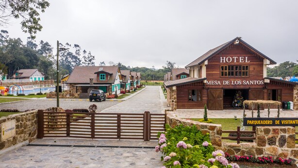 A rustic hotel with a wooden facade, a sign reading "HOTEL MESA DE LOS SANTOS," and a gated entrance.