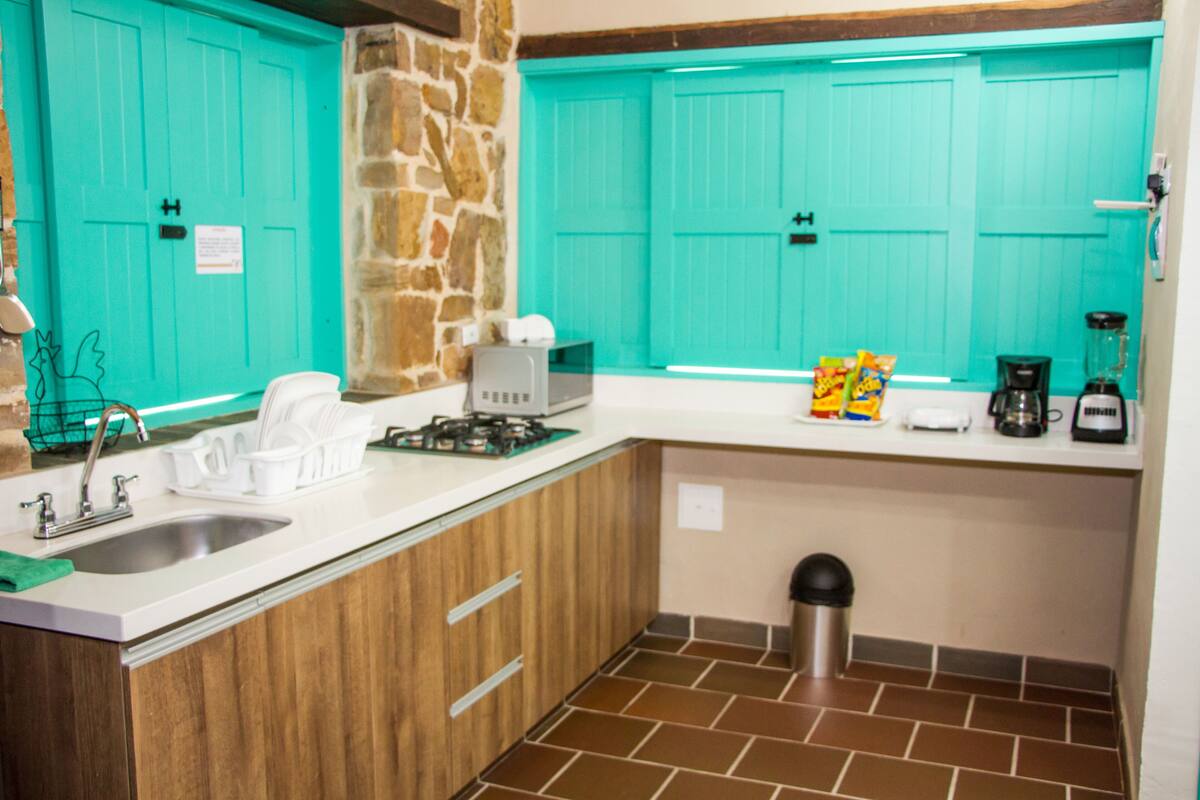A kitchen with turquoise cabinets, a stone accent wall, a sink, a stove, and a coffee maker.