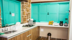 A kitchen with turquoise cabinets, a stone accent wall, a sink, a stove, and a coffee maker.