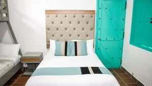A hotel room with a bed, a nightstand, a teal door, and a white wall.