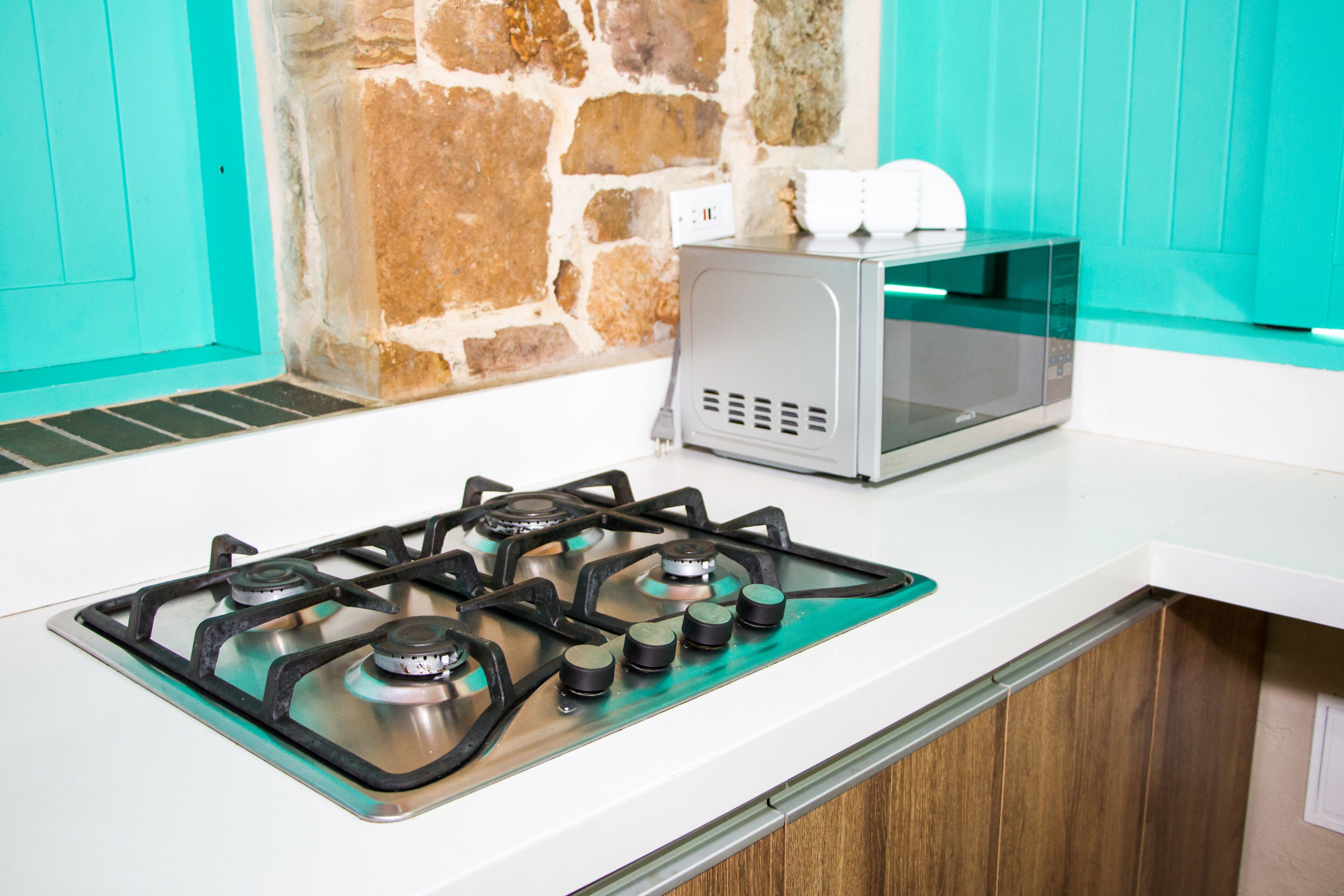 A kitchen with a gas stove, a microwave, and a stone wall.
