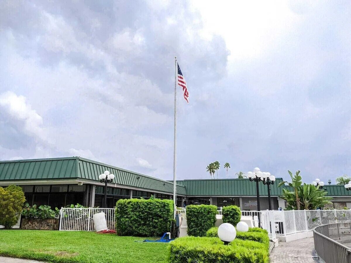 A building with a green roof, a flagpole with an American flag, and a well-maintained lawn with bushes and a pathway.