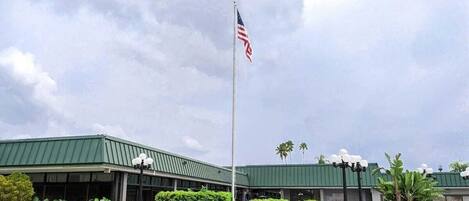 A building with a green roof, a flagpole with an American flag, and a well-maintained lawn with bushes and a pathway.
