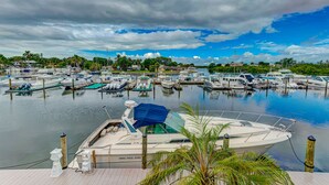 A marina with multiple boats docked, surrounded by greenery and a cloudy sky.
