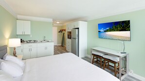 A hotel room with a bed, a desk, a chair, a TV, and a kitchen area.