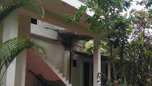 A two-story building with a covered porch, a staircase leading to the upper floor, and a small garden area with a tree and a potted plant. - La Jungle Vista sigiriya (Sigiriya)