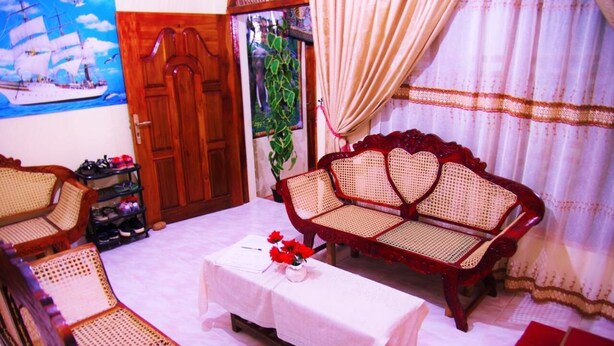 A room with a wooden door, a rattan sofa, a matching armchair, a small table with a vase of flowers, and a shoe rack. - La Jungle Vista sigiriya (Sigiriya)