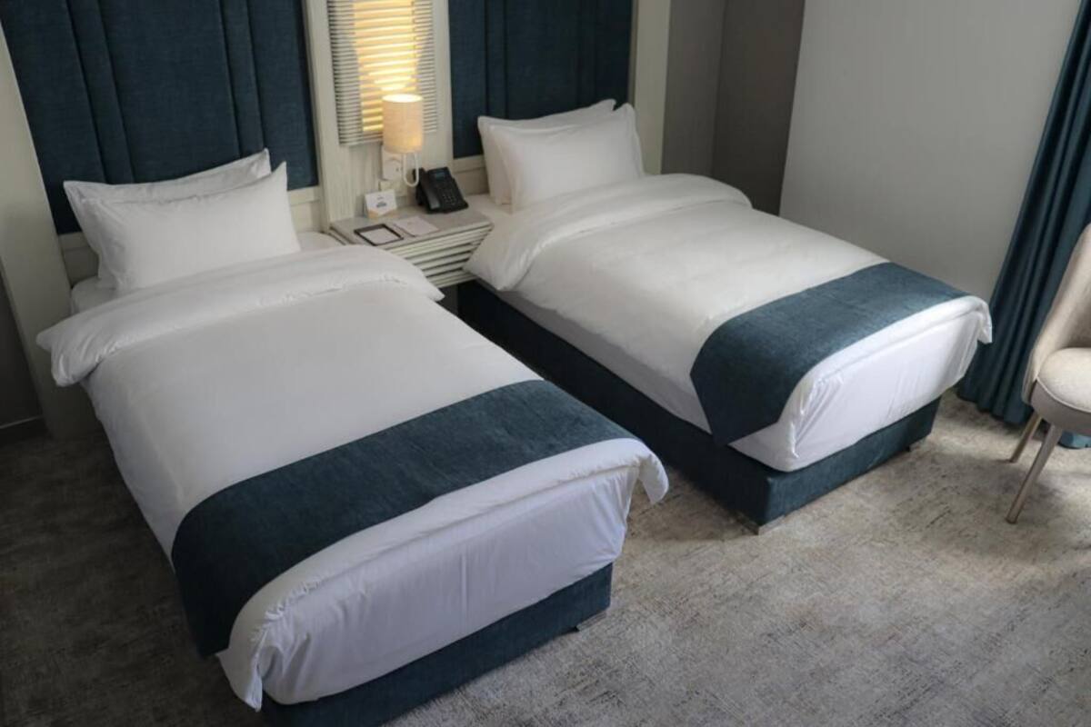 Una camera d'albergo con due letti, un comodino con una lampada e una sedia.