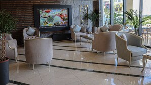 Un vestíbulo con una gran pantalla mostrando comida, asientos cómodos y vistas de la ciudad a través de amplias ventanas.