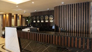 A reception desk with a modern design, featuring a black and white marble pattern, a laptop, and a potted plant.